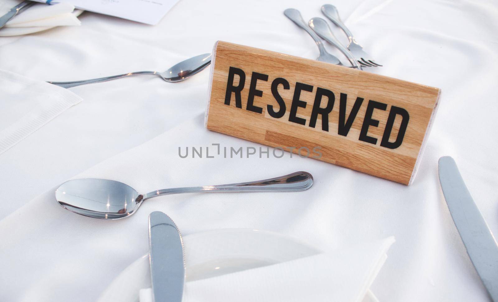A wooden Reserved sign on a restaurant table with a white tablecloth and shiny cutlery