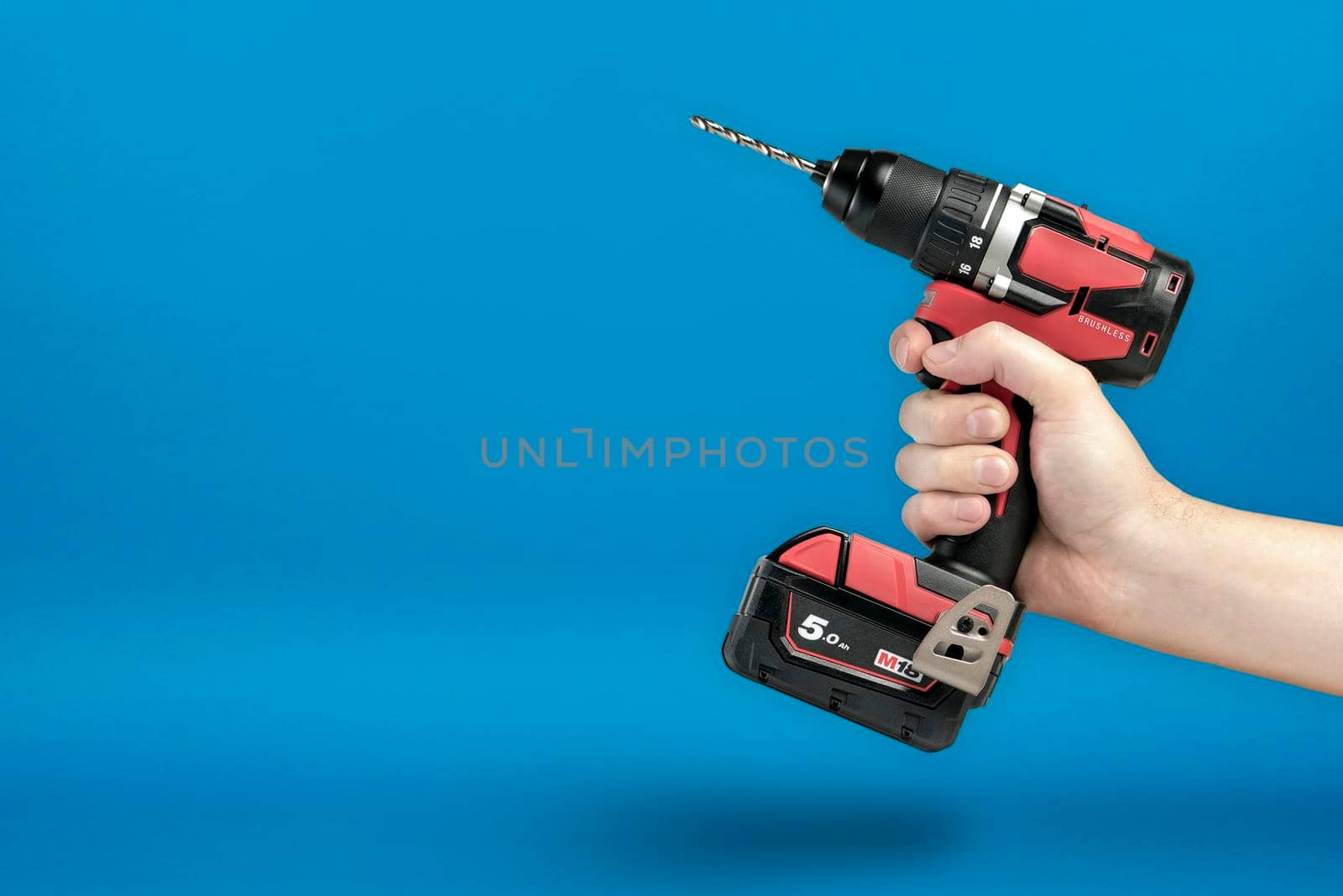 Cordless screwdriver in hand. Cordless tool in a man's hand. The concept of repair and construction on a blue background. by SERSOL