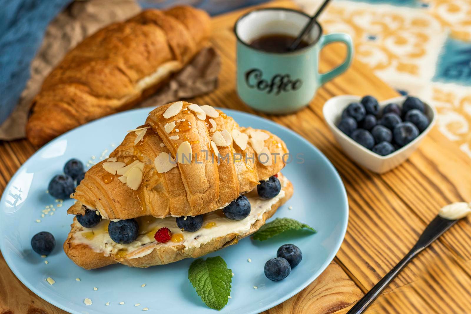 classic american breakfast. Fresh french croissant with fresh berries. blueberry and strawberry on cream cheese. Croissant and a cup with the inscription coffee on wooden background. Healthy breakfast