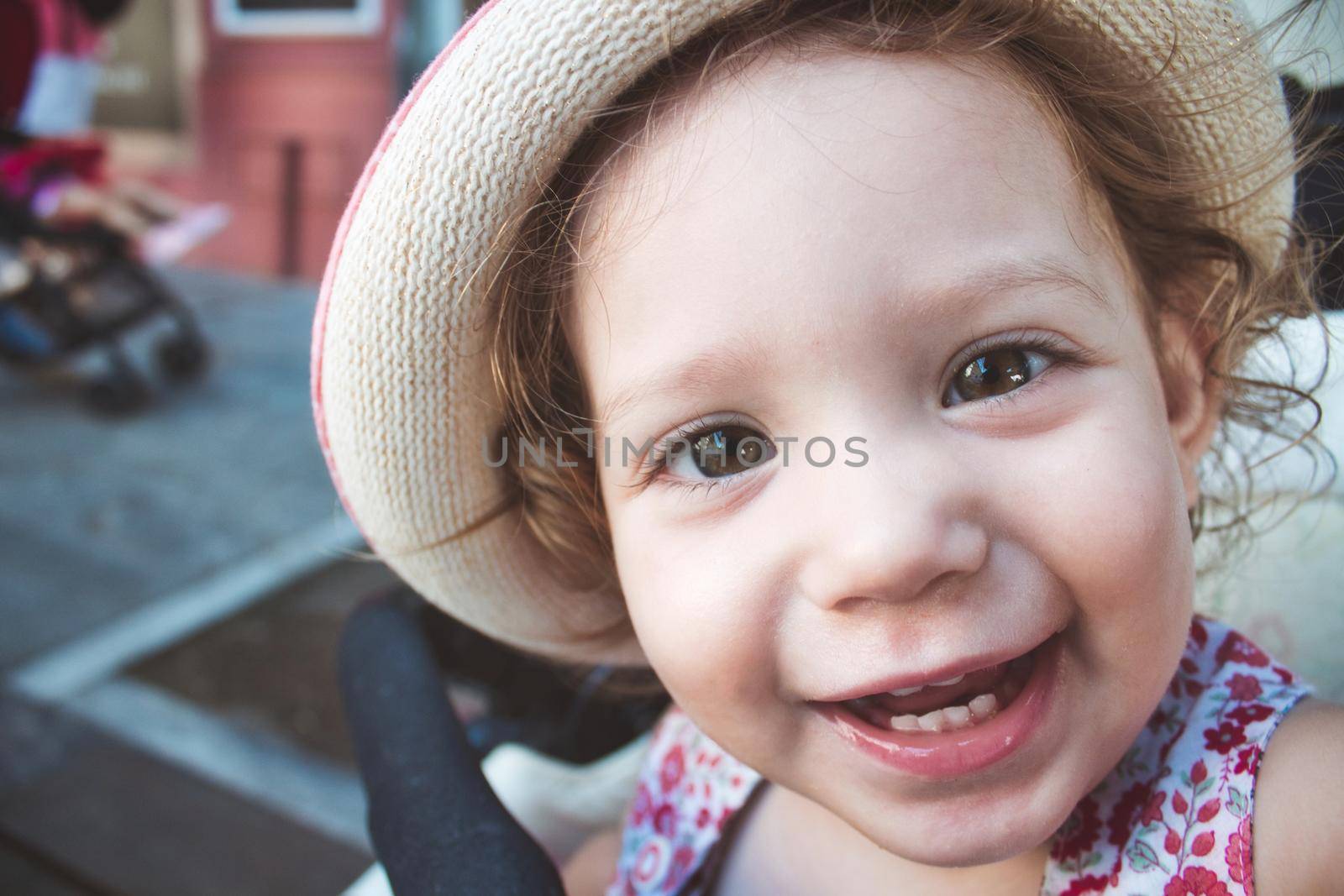 Close-up portrait of cute baby girl looking at camera smiling and wearing a hat by tennesseewitney