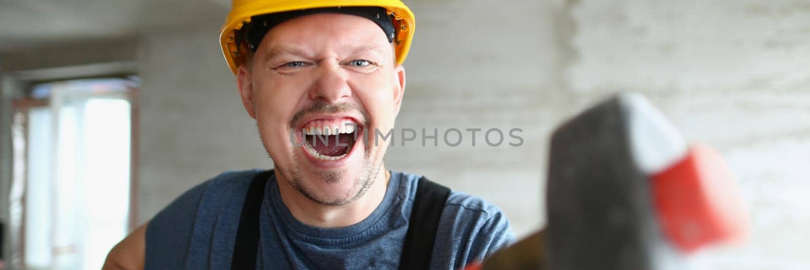 Builder man with a long hammer in his hands, close-up. Disassembly with a sledgehammer. Building renovation, cheerful handyman