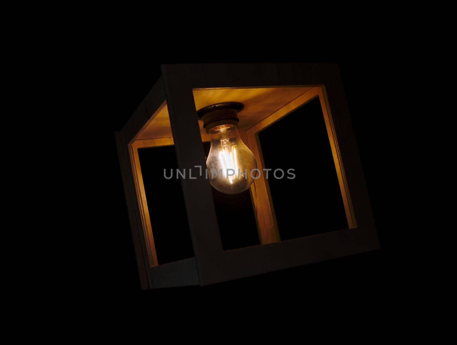 Warm yellow glowing light bulb encased in a wooden box against a black background by tennesseewitney