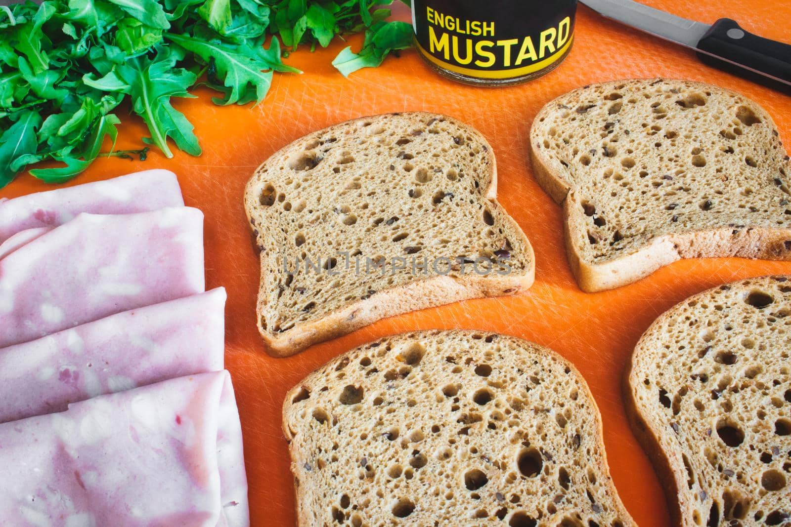 Slices of wholemeal brown bread laid out on a chopping board with ham, rocket and English mustard by tennesseewitney