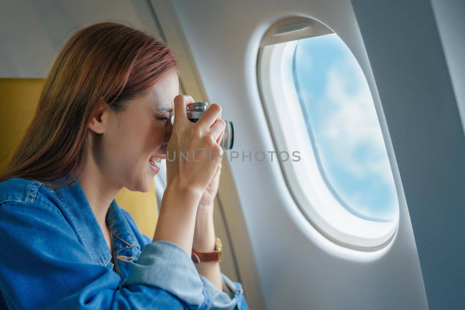 Travel, Portrait of a smiling Asian female tourist with a camera taking pictures of the sky during her flight by Manastrong