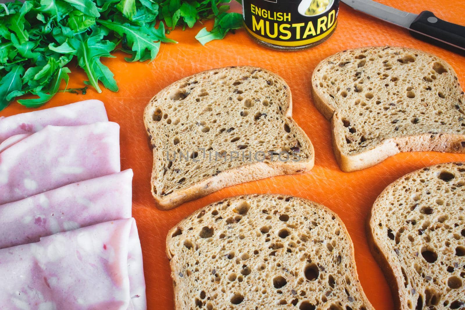 Slices of wholemeal brown bread laid out on a chopping board with ham, rocket and English mustard by tennesseewitney