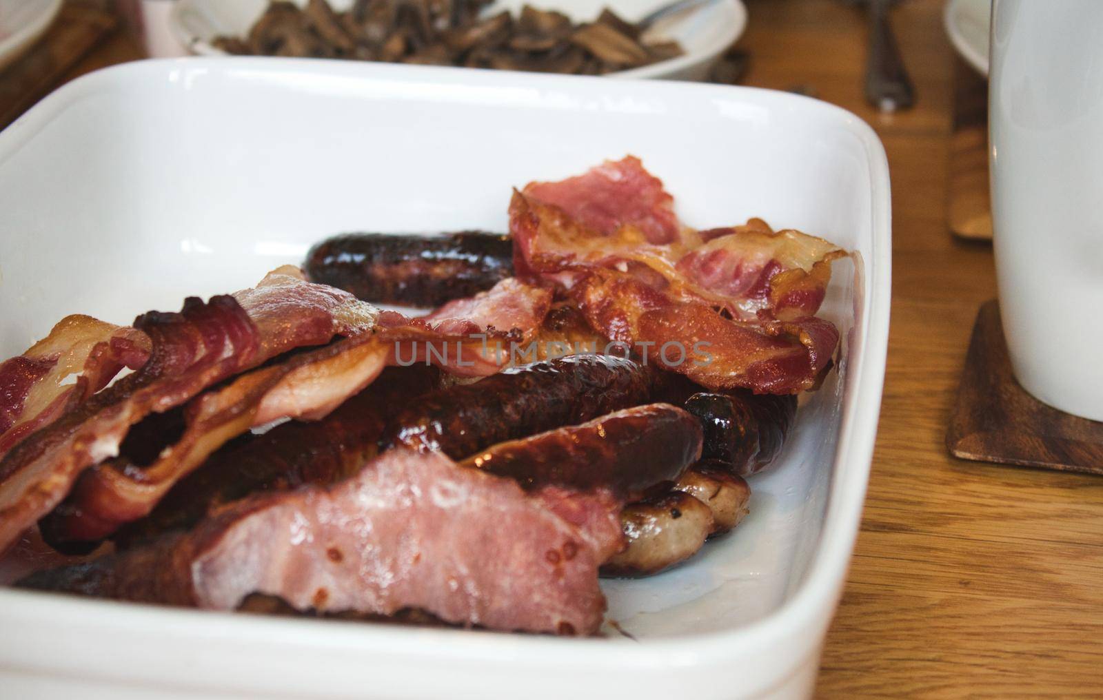 Greasy fried bacon and sausages on a white ceramic plate - typical English breakfast by tennesseewitney
