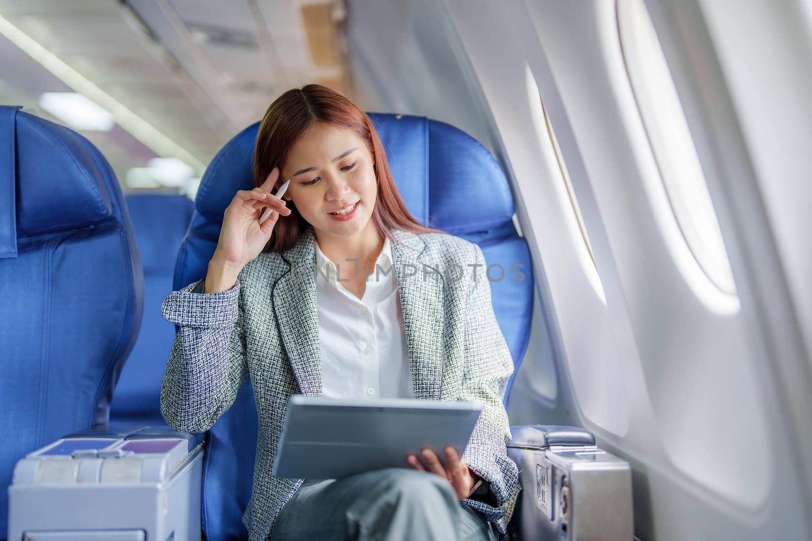 Travel, Portrait of an Asian business woman using tablet computer to plan while on a plane between waiting to negotiate business with foreign investors by Manastrong