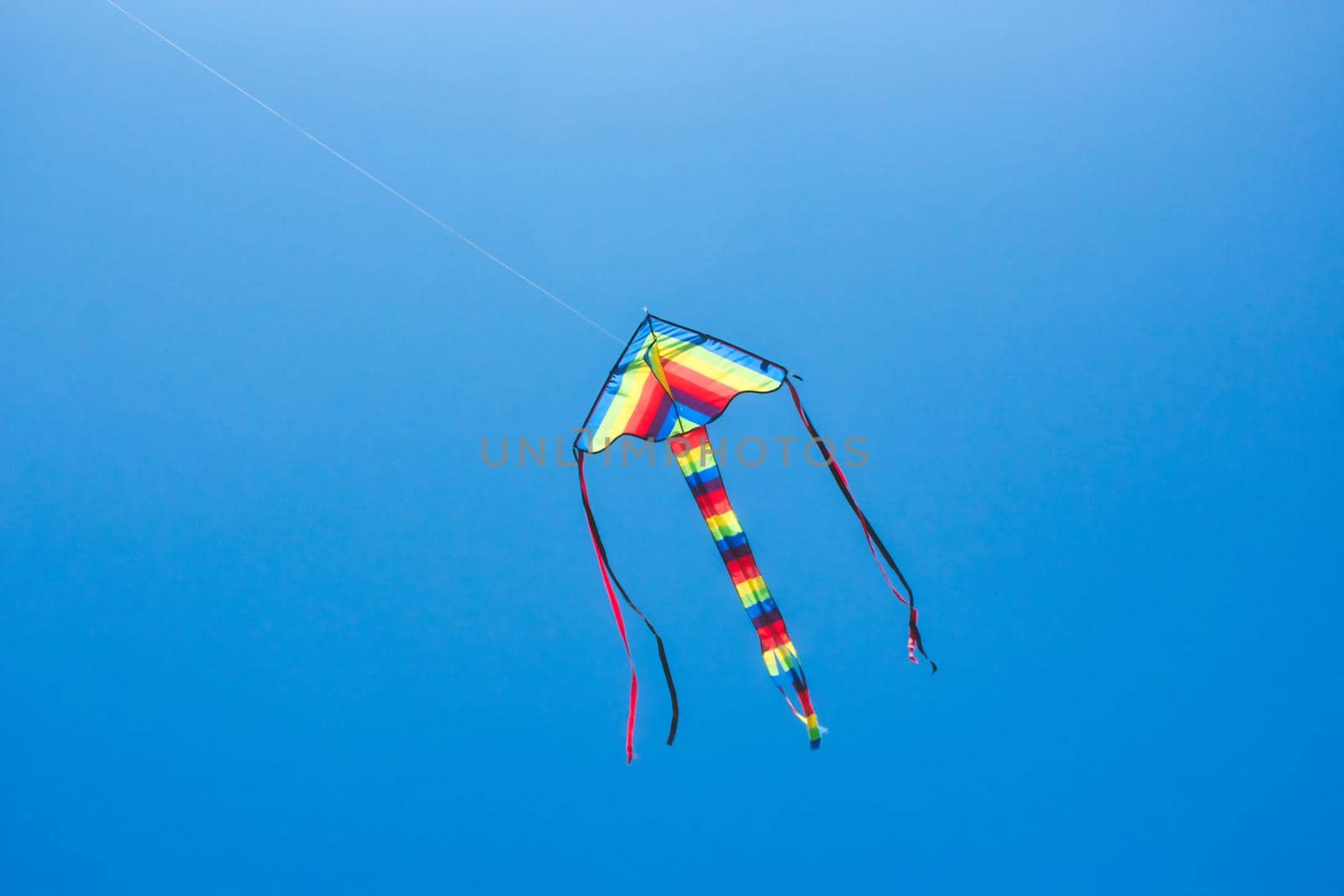 A colourful kite flying in a clear blue sky with a long tail and streamers