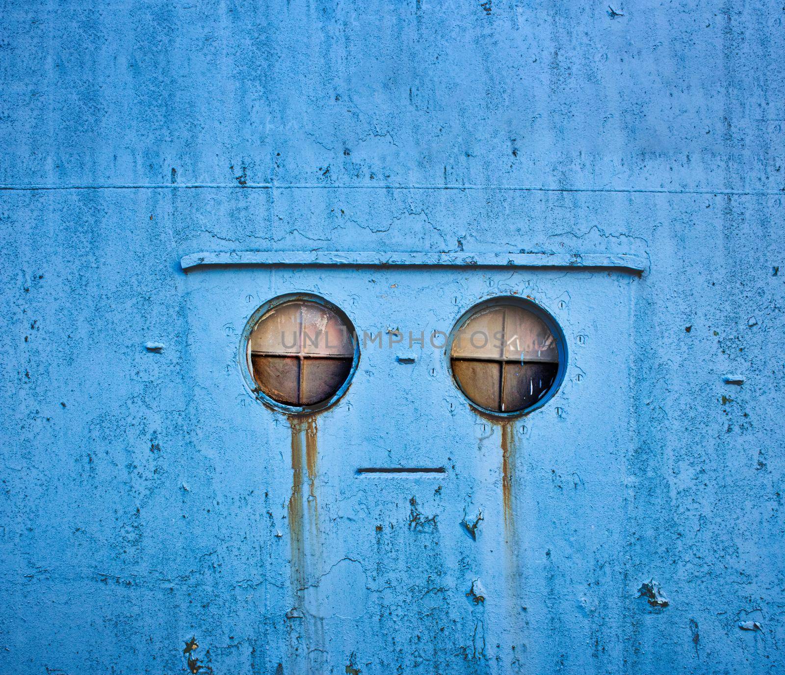 A robotic mechanical face shedding tears in a blue metallic industrial wall