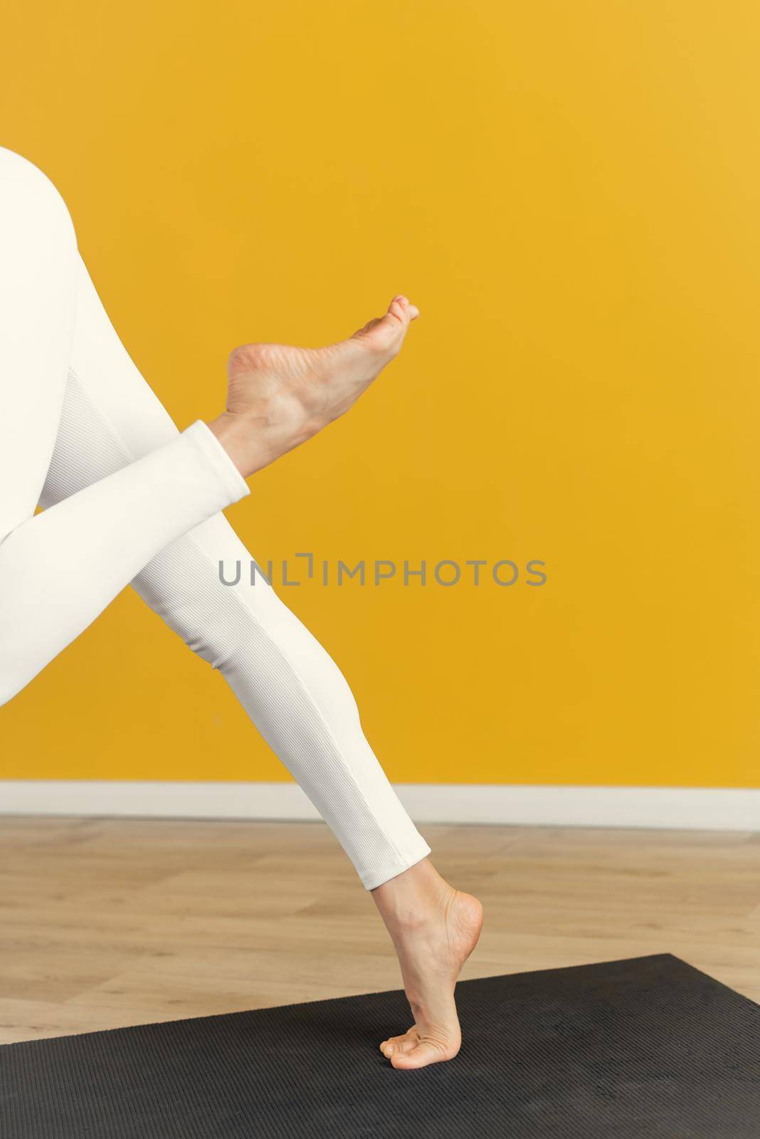 Women's legs in a yoga pose on a yellow background. Close up. Leg stretching concept.