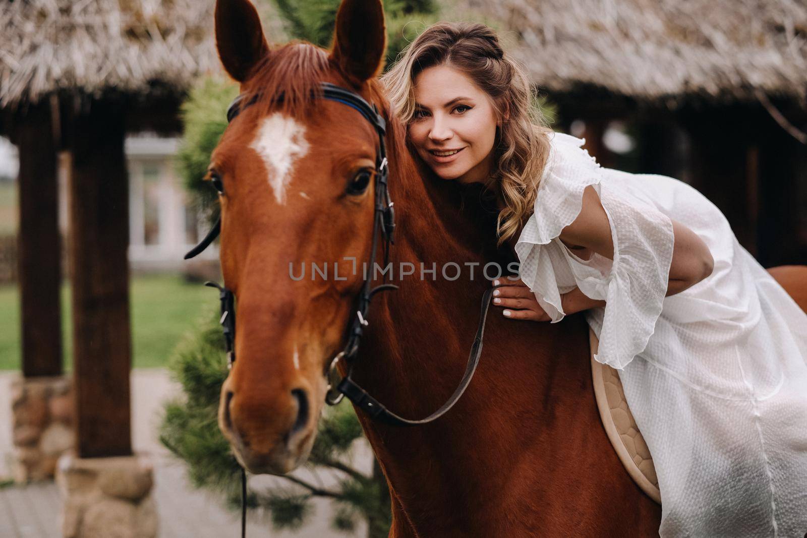 A woman in a white sundress riding a horse near a farm.