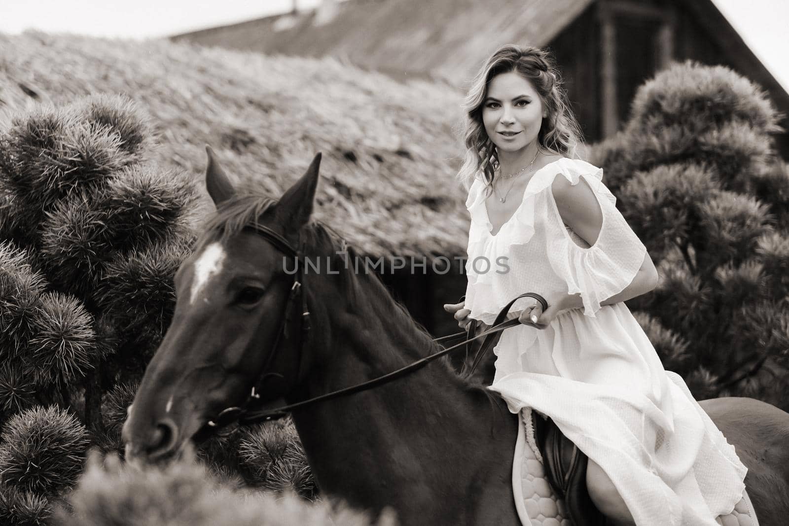 A woman in a white sundress riding a horse near a farm. black and white photo by Lobachad