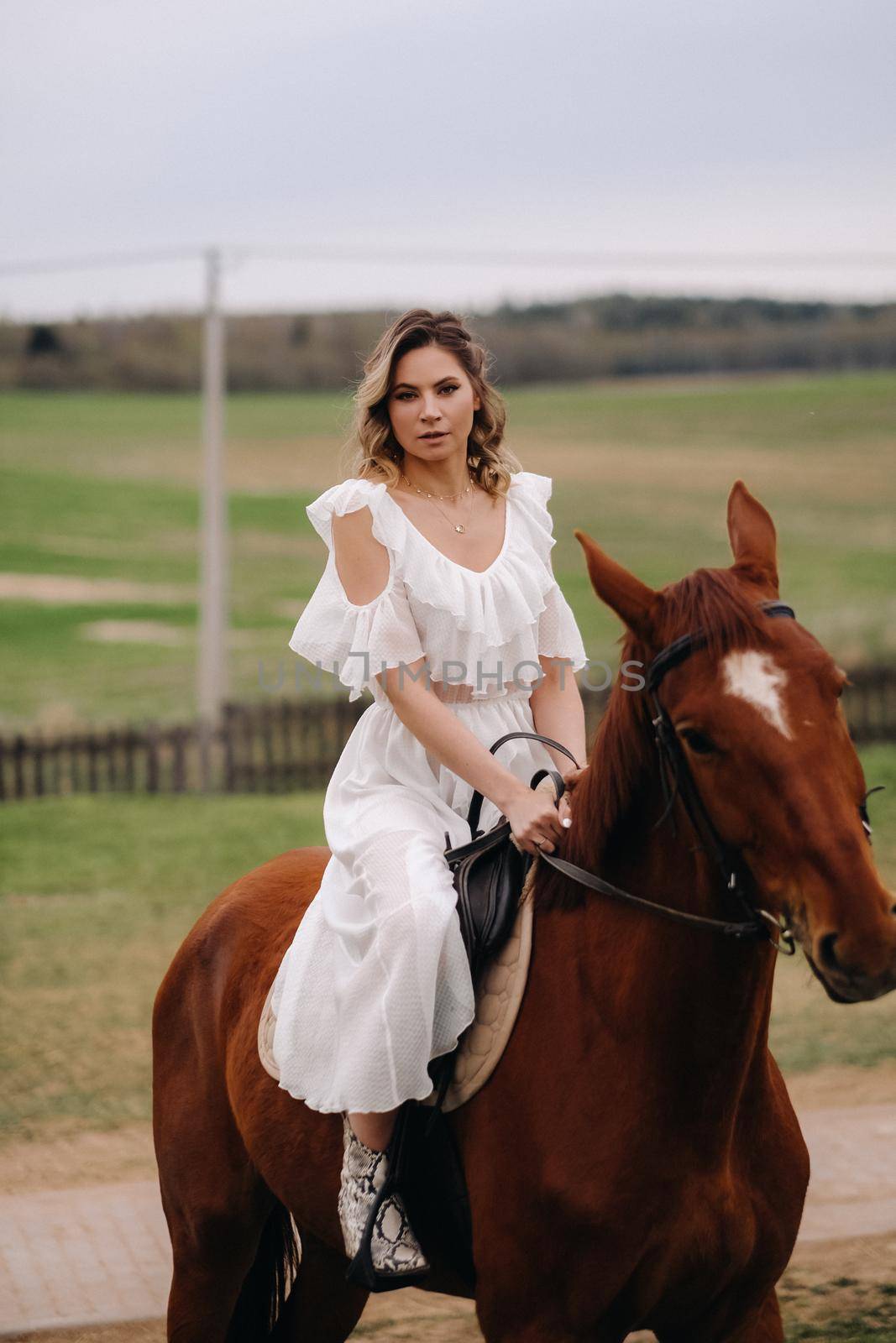 A woman in a white sundress riding a horse in a field.