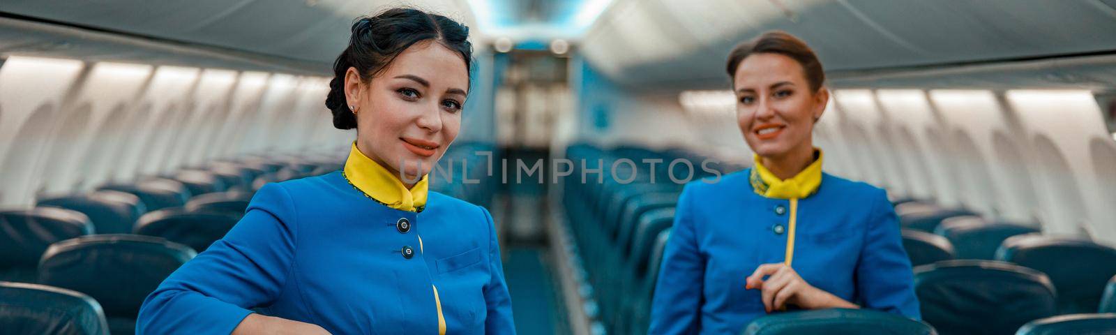 Cheerful stewardesses standing in aircraft passenger salon by Yaroslav_astakhov