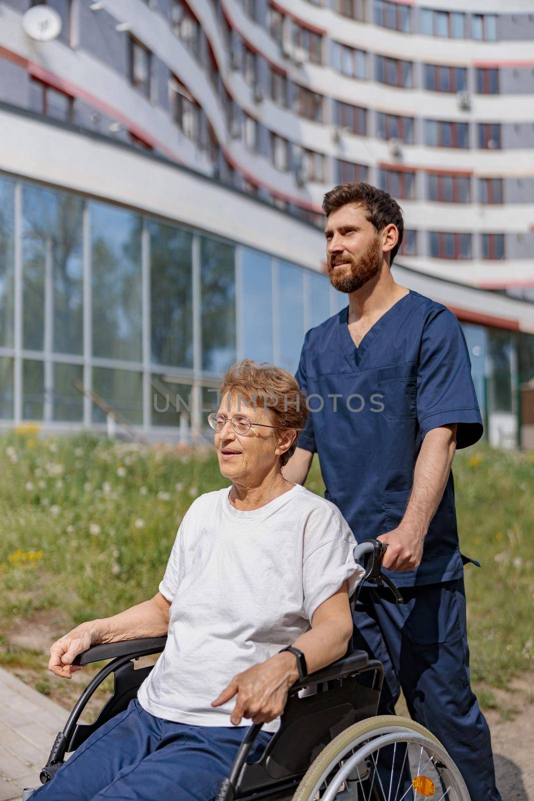 Nurse talking to patient on wheelchair in hospital yard . Rehabilitation concept.