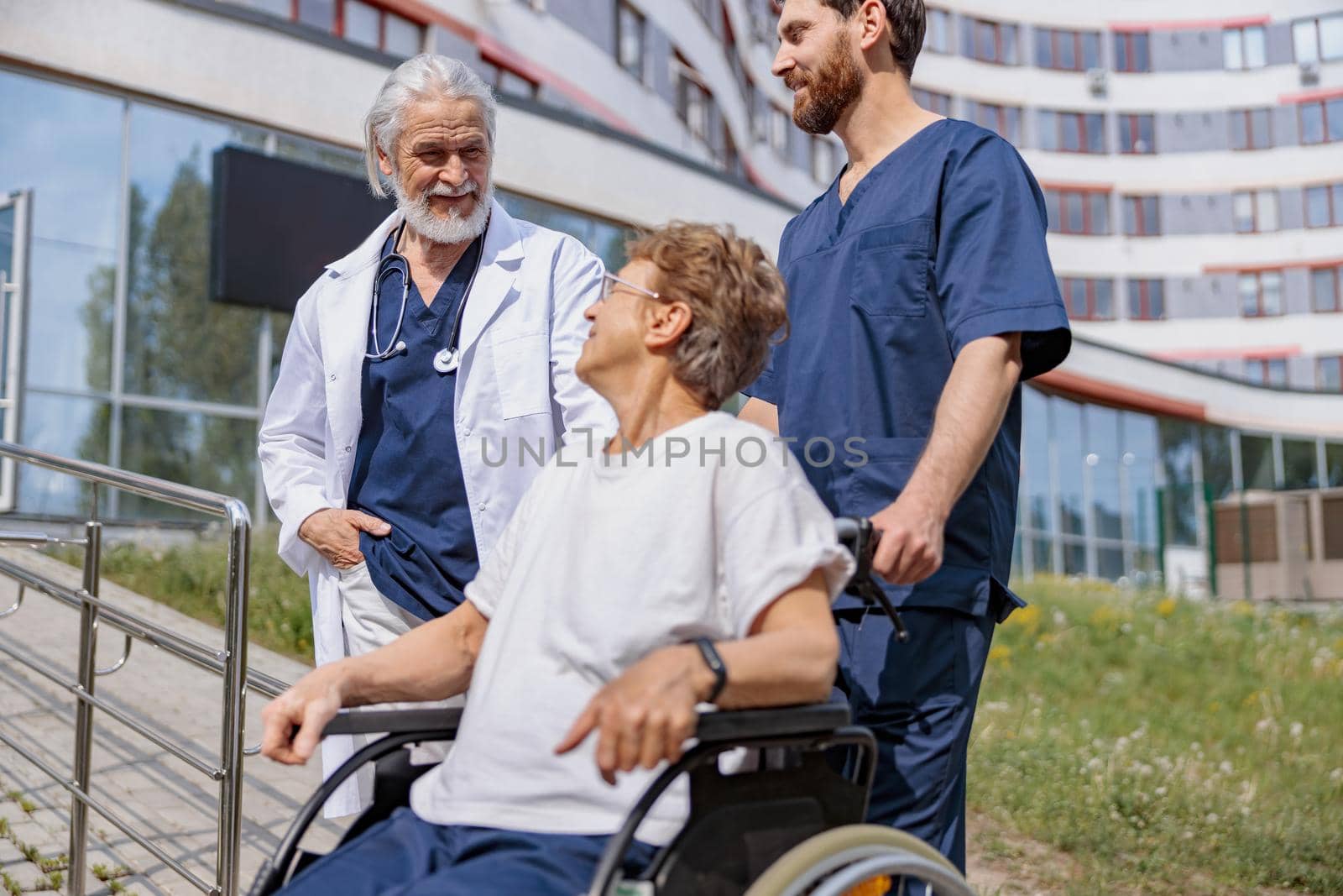 Nurse and doctor talking to patient on wheelchair in hospital yard . Rehabilitation concept.