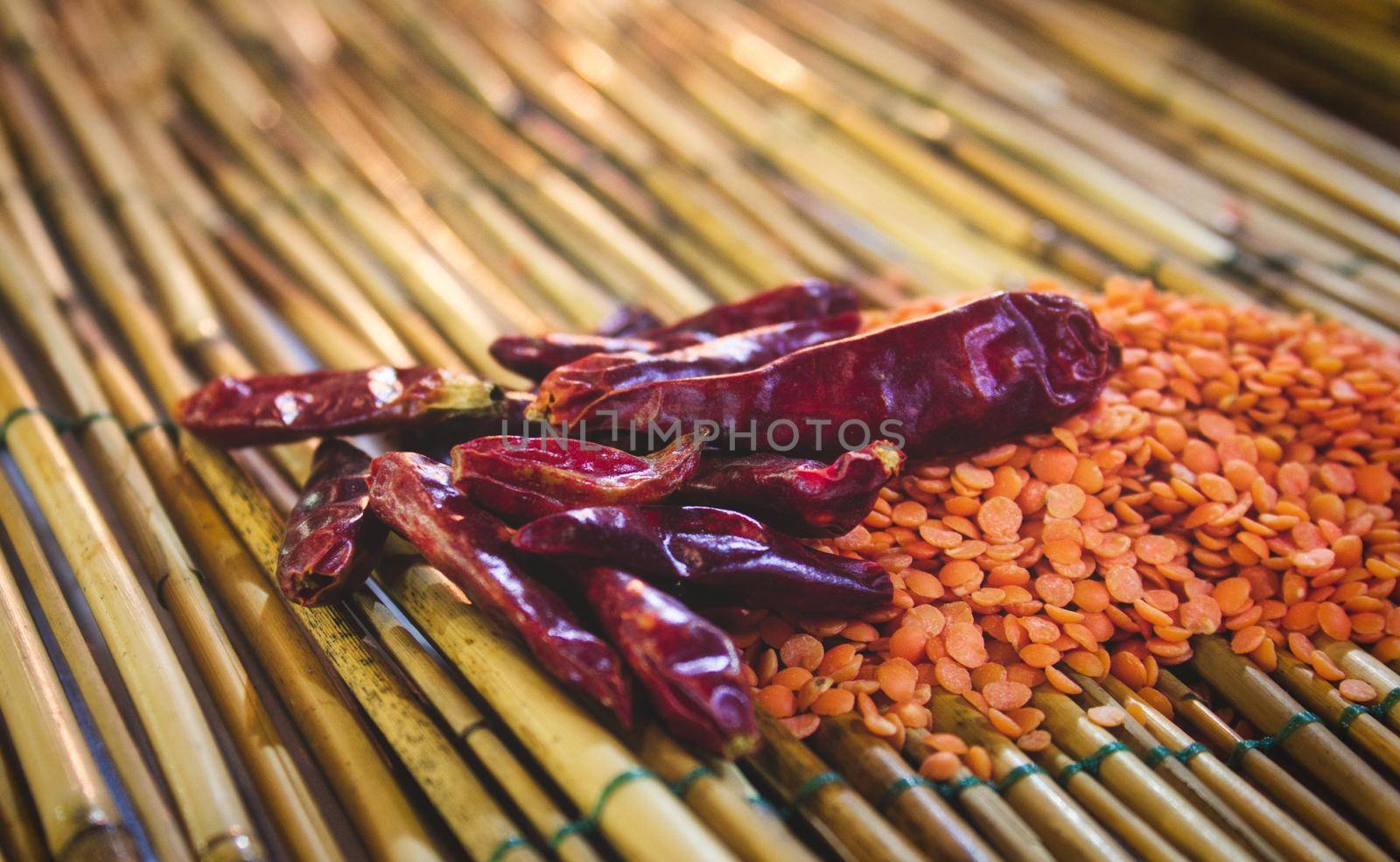 Chili peppers (Capsicum annuum) and red lentils on a bamboo mat by tennesseewitney