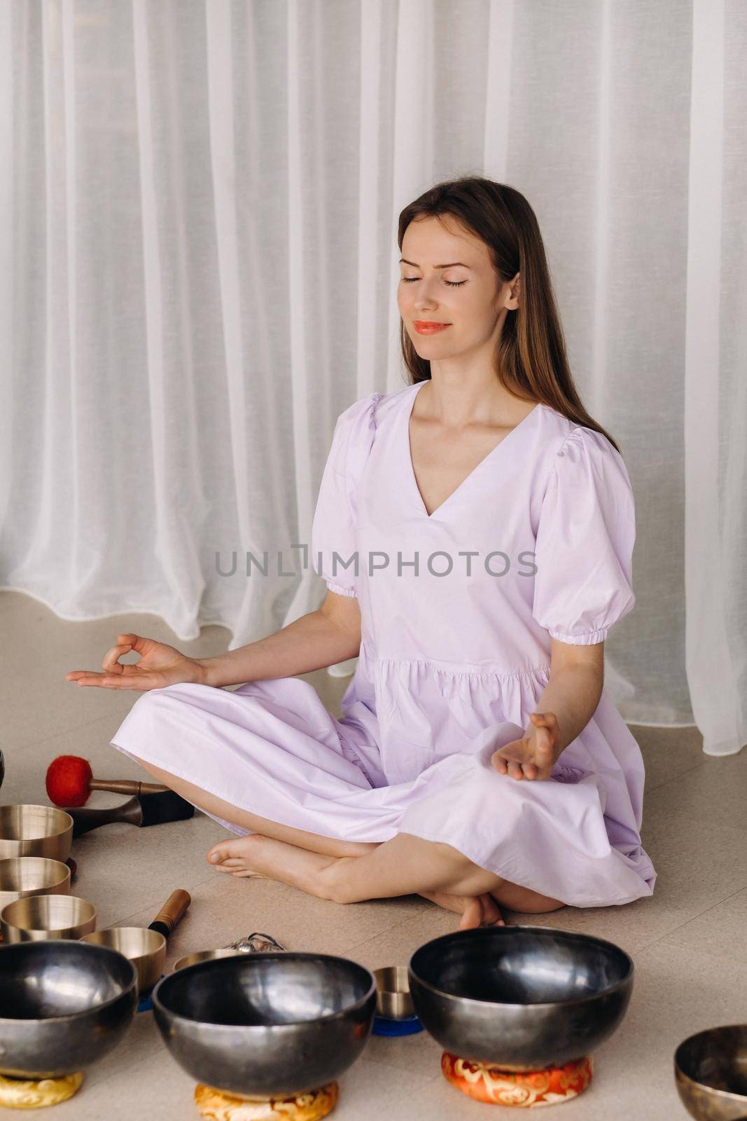 A woman sits with Tibetan bowls in the lotus position before doing yoga in the gym.