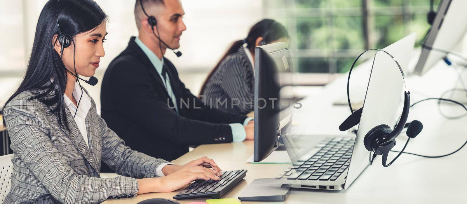 Business people wearing headset working in office to support remote customer or colleague. Call center, telemarketing, customer support agent provide service in broaden view .