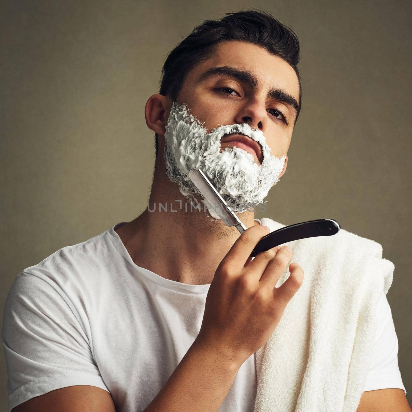 Cropped shot of a handsome young man shaving with a straight razor.