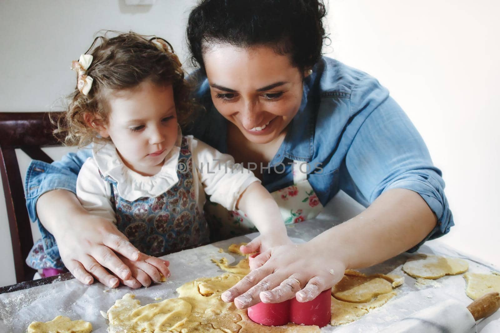 Mother and daughter baking cookies in the kitchen - cutting pastry dough with plastic shape cutters by tennesseewitney
