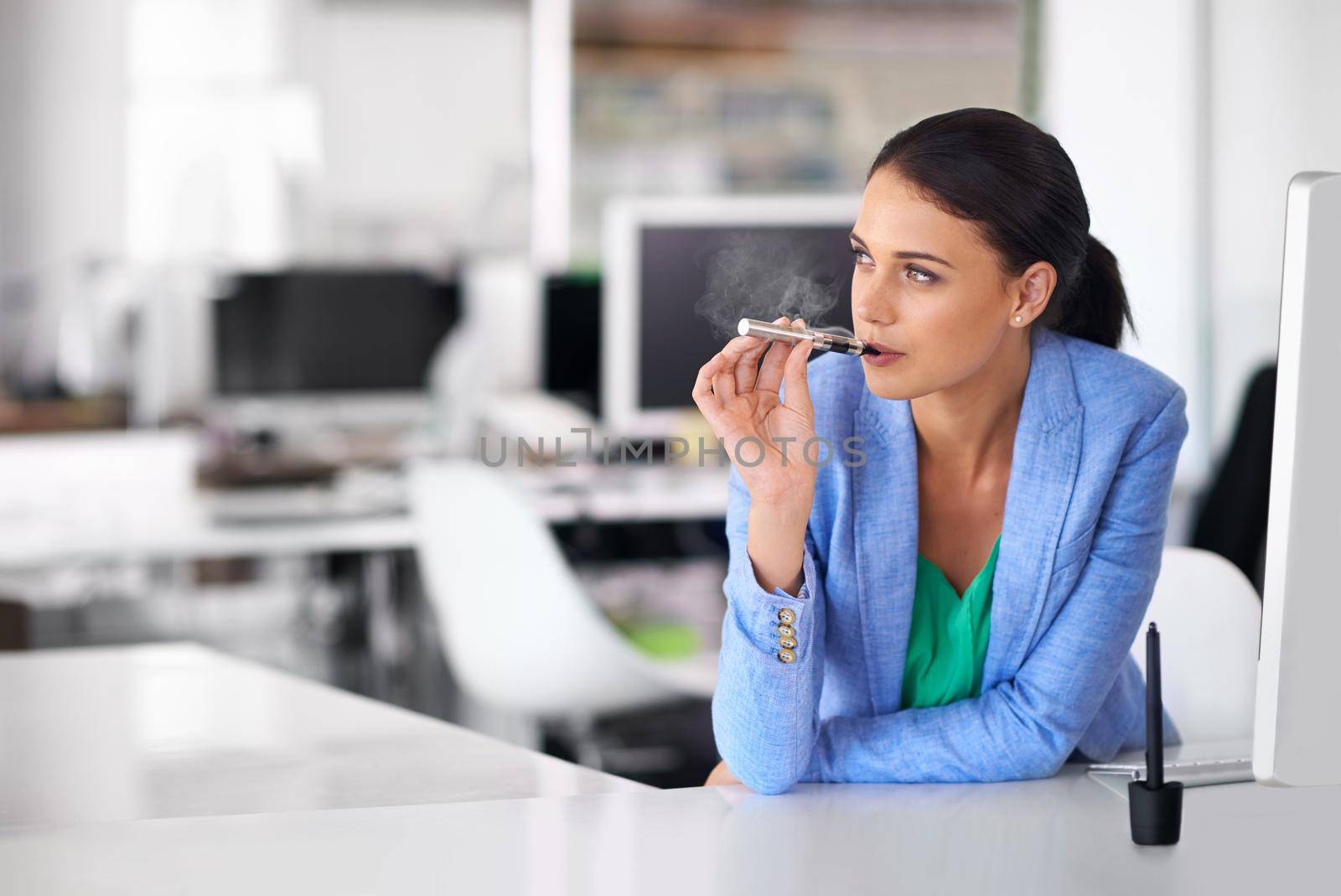 Having a quick vape between meetings. Shot of a businesswoman smoking and electronic cigarette in an office. by YuriArcurs