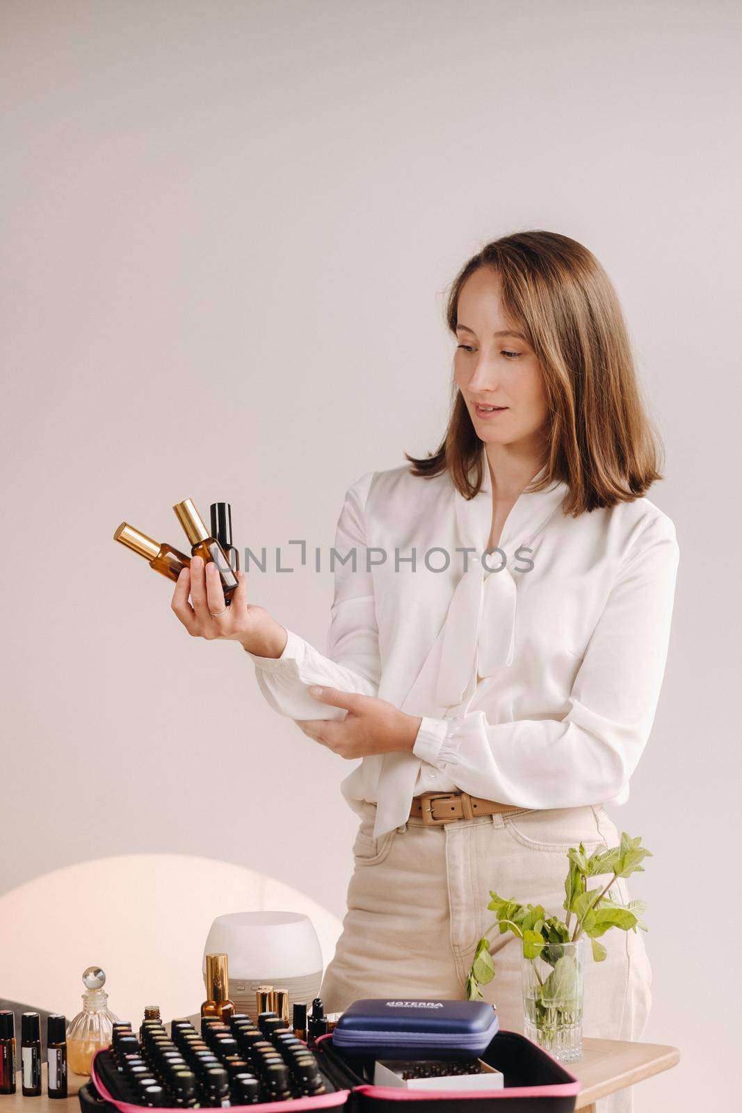 A girl with a white blouse holds bottles of essential oils in her hands.