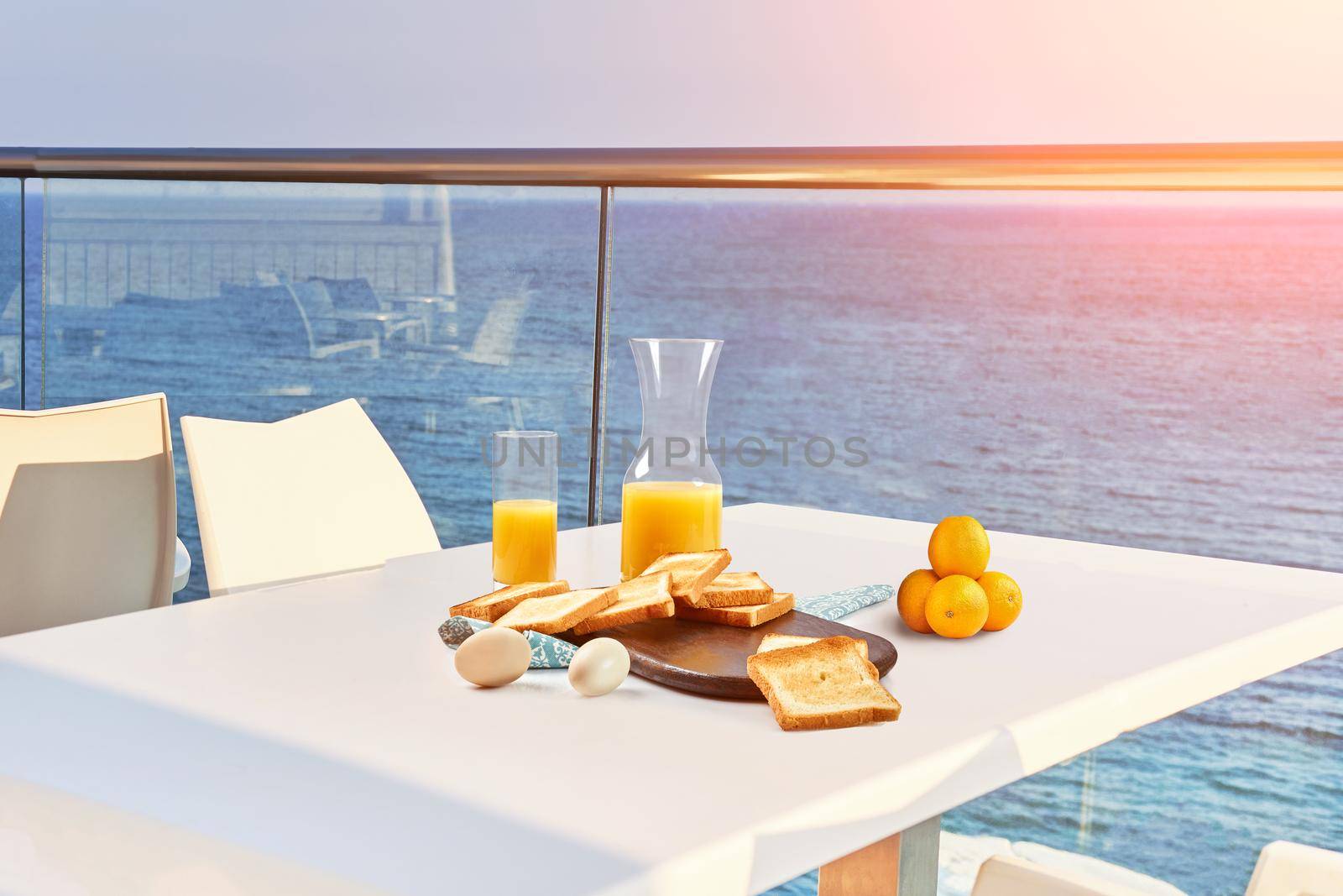 Table for two on outdoor hotel balcony with a sea view. European vacation breakfast, food selfie with a sunflare. Concept of a rest and healthy nutrition. There are toasts, eggs, orange juice.