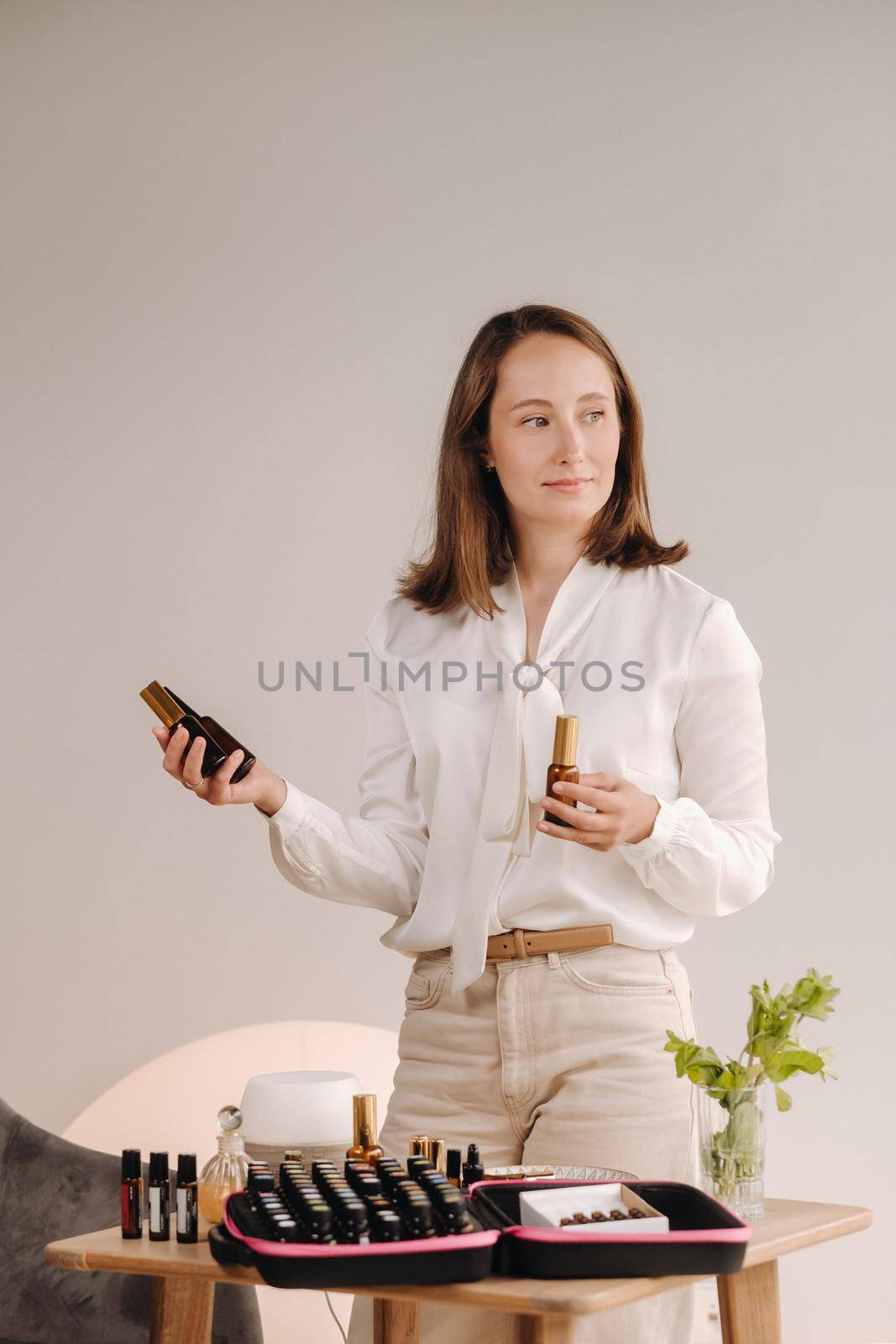 A girl with a white blouse holds bottles of essential oils in her hands.