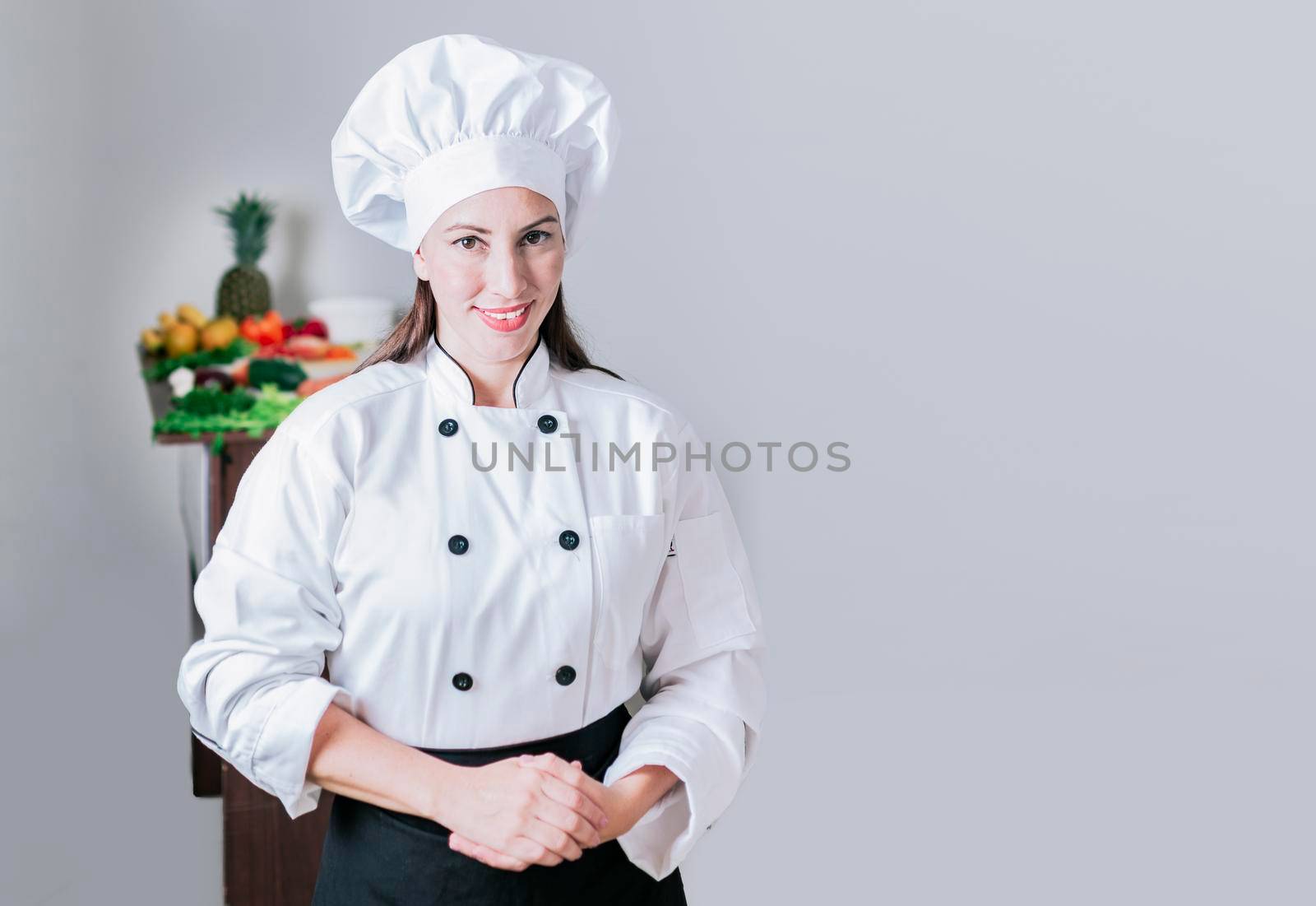 Portrait of a female chef surrounded by fresh vegetables, Portrait of a female nutritionist in uniform with fresh vegetables on the table, A female nutritionist with a table of vegetables by isaiphoto