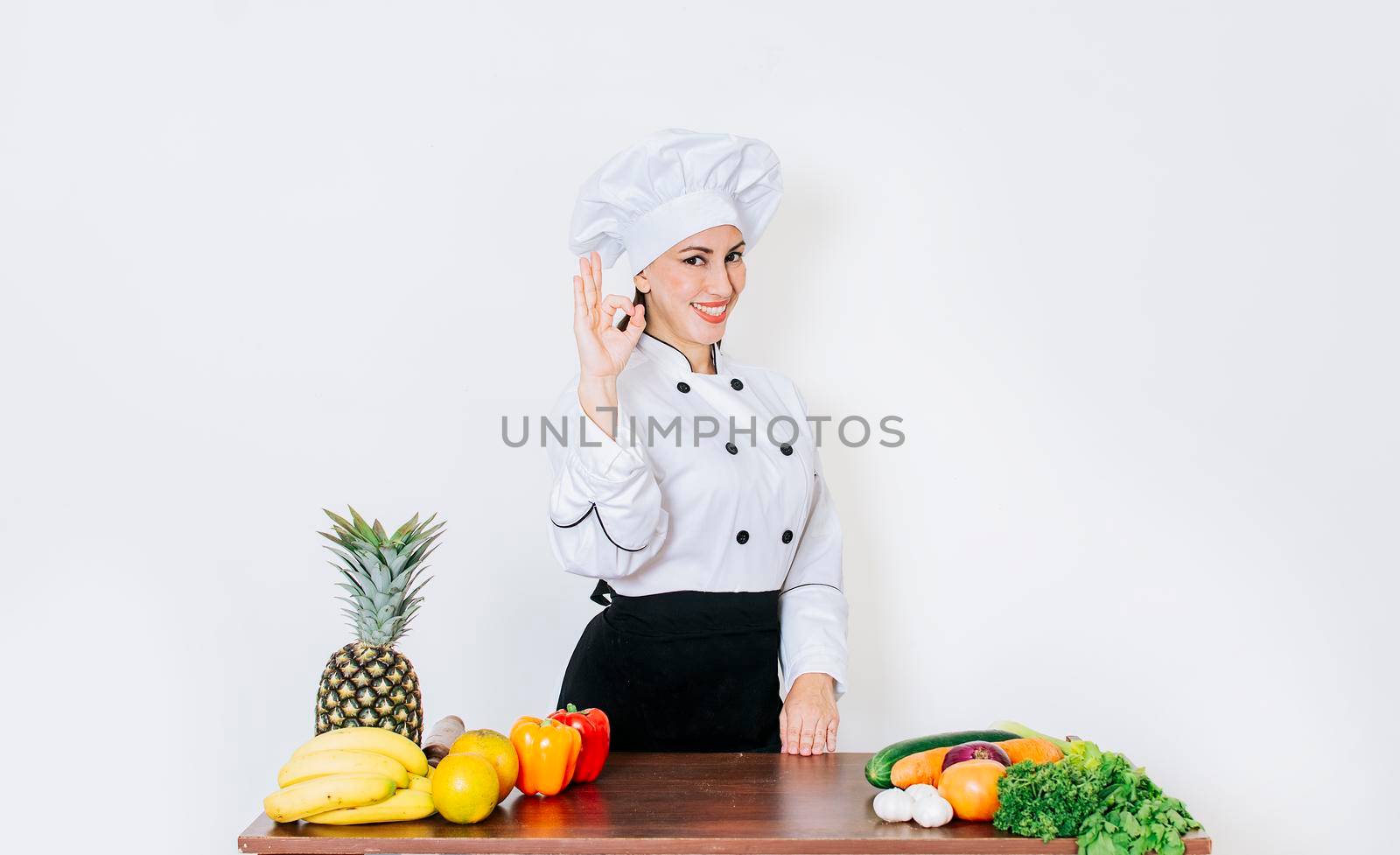 Woman chef making ok gesture, a woman chef at a vegetable table with thumbs up, Concept of a woman chef recommending fresh vegetables by isaiphoto