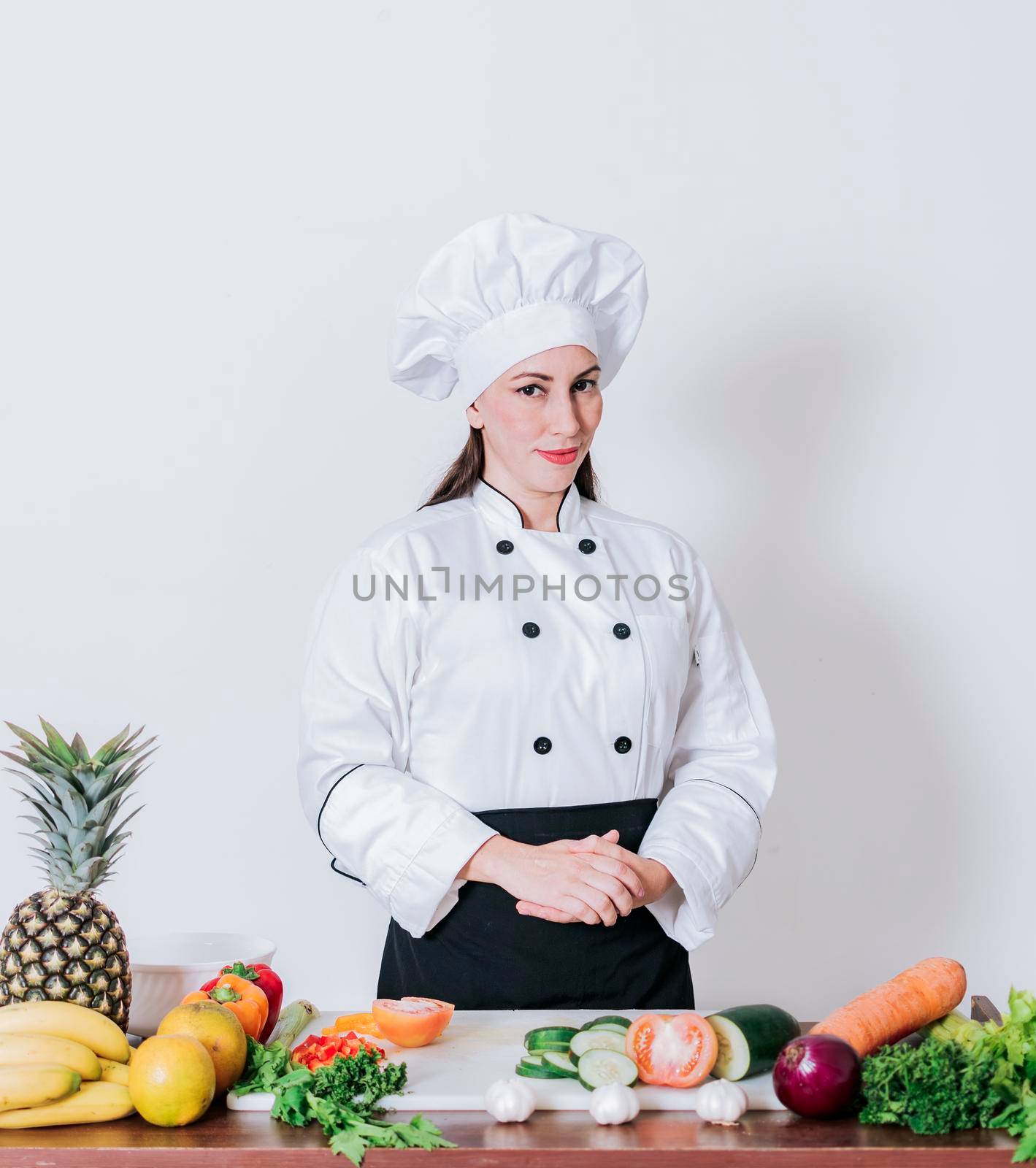 Portrait of a female chef surrounded by fresh vegetables, Portrait of a female chef with fresh vegetables on the table, A female nutritionist with a table of vegetables by isaiphoto