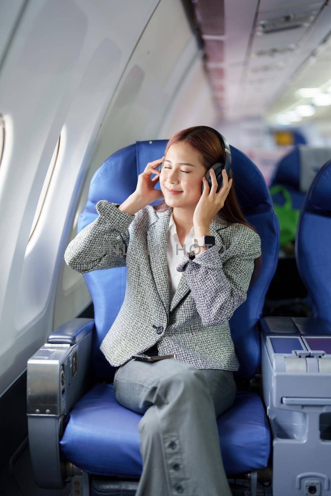 Travel, Portrait of an Asian business woman listening to music while on a plane between waiting to negotiate business with foreign investors by Manastrong
