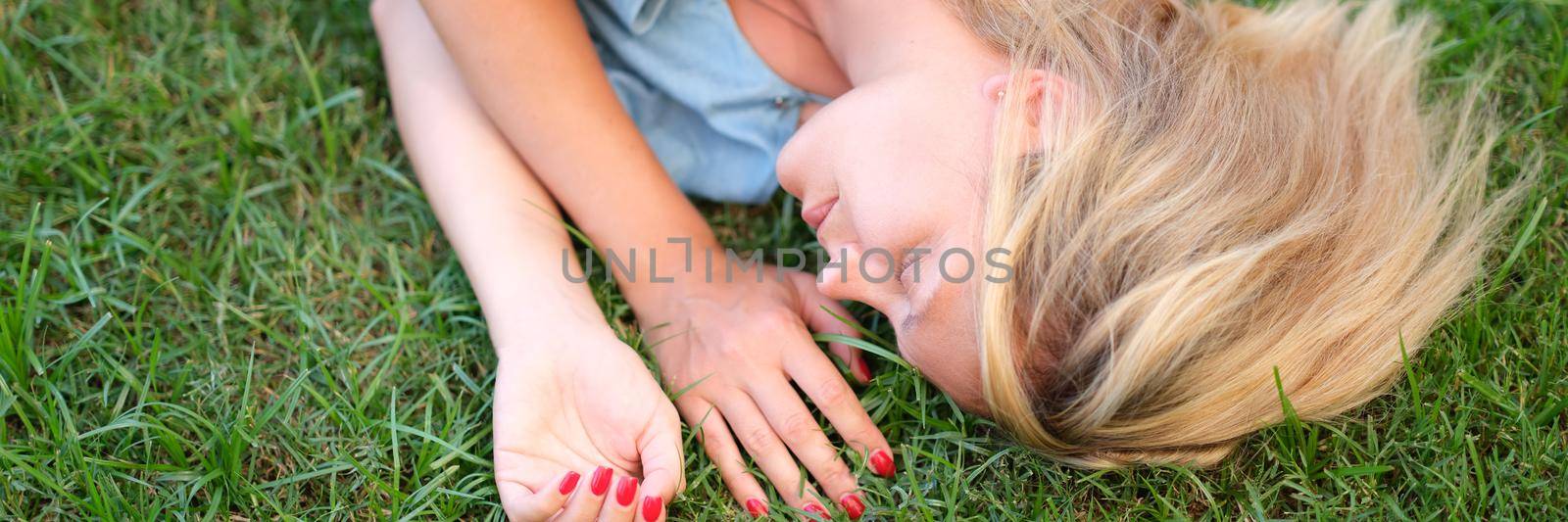 A young woman in a dress is sleeping on the green grass, close-up. Unity with nature, healthy ecology, relaxation