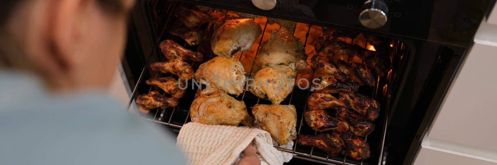 The woman determines the readiness of the chicken in the oven, close-up, blurry. BBQ cooking, grill wings