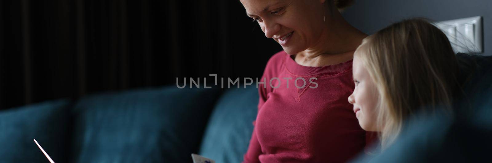 A woman with a child on the couch pays for online purchases, close-up. Online grocery ordering during a pandemic