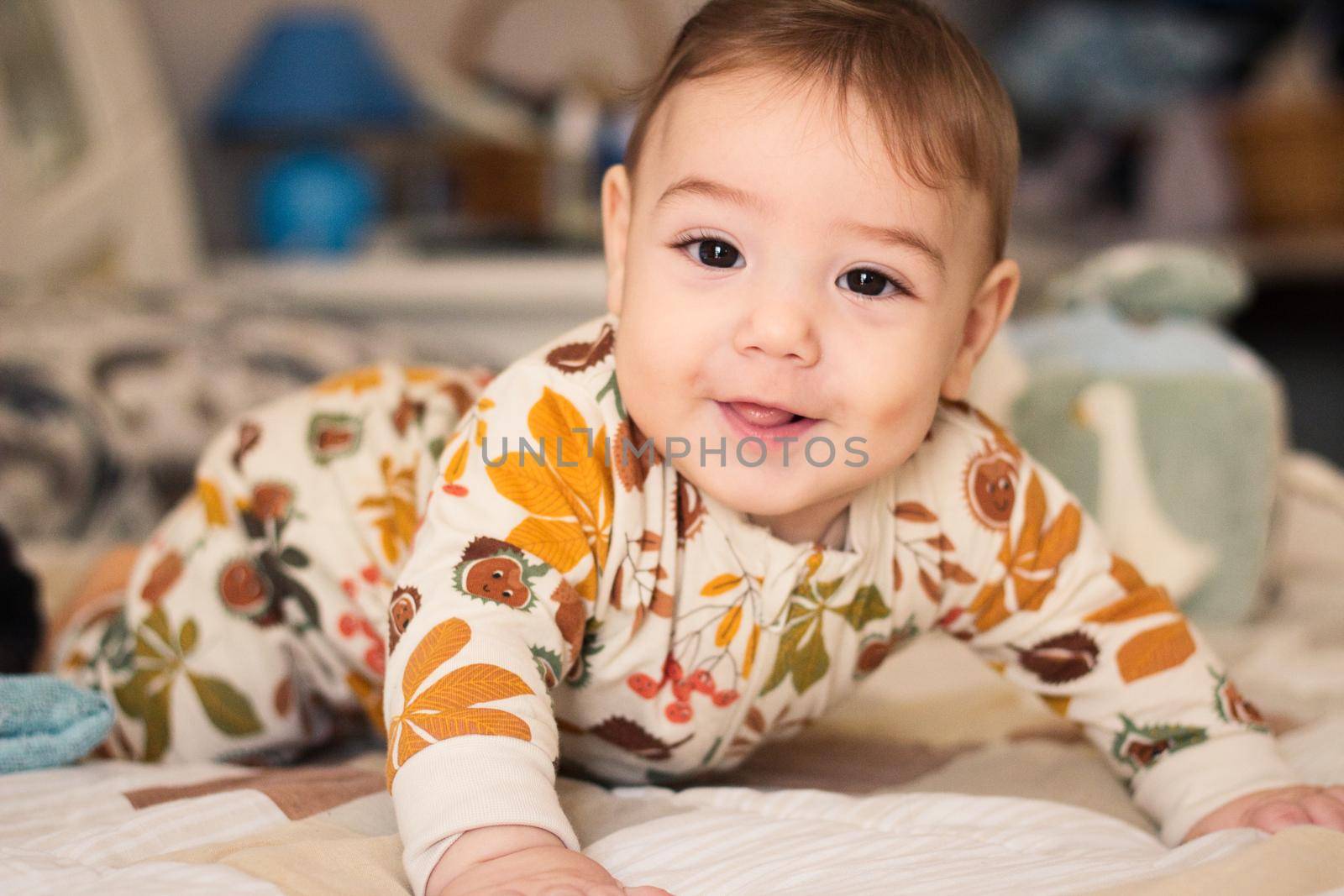 Cute baby on a bed wearing a romper suit pajama onesie looking directly at the camera
