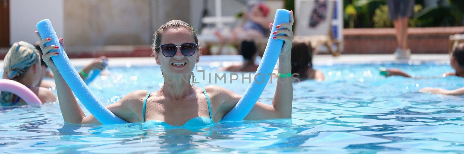 Happy woman swims in the outdoor summer pool. Aqua aerobics, healthy recreation at the resort, aquafitness