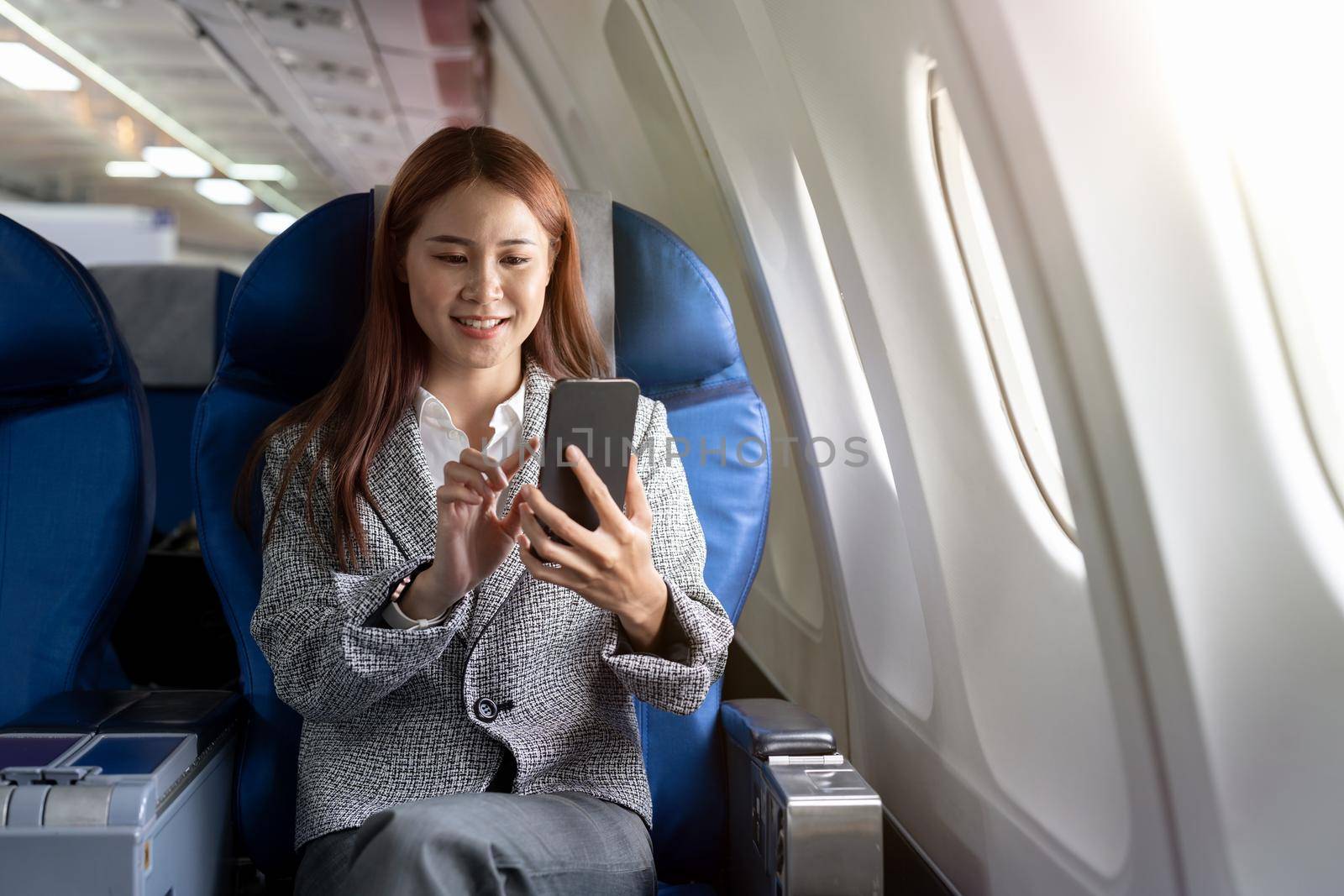 Travel and technology. Young woman in plane using smartphone while sitting in airplane seat.