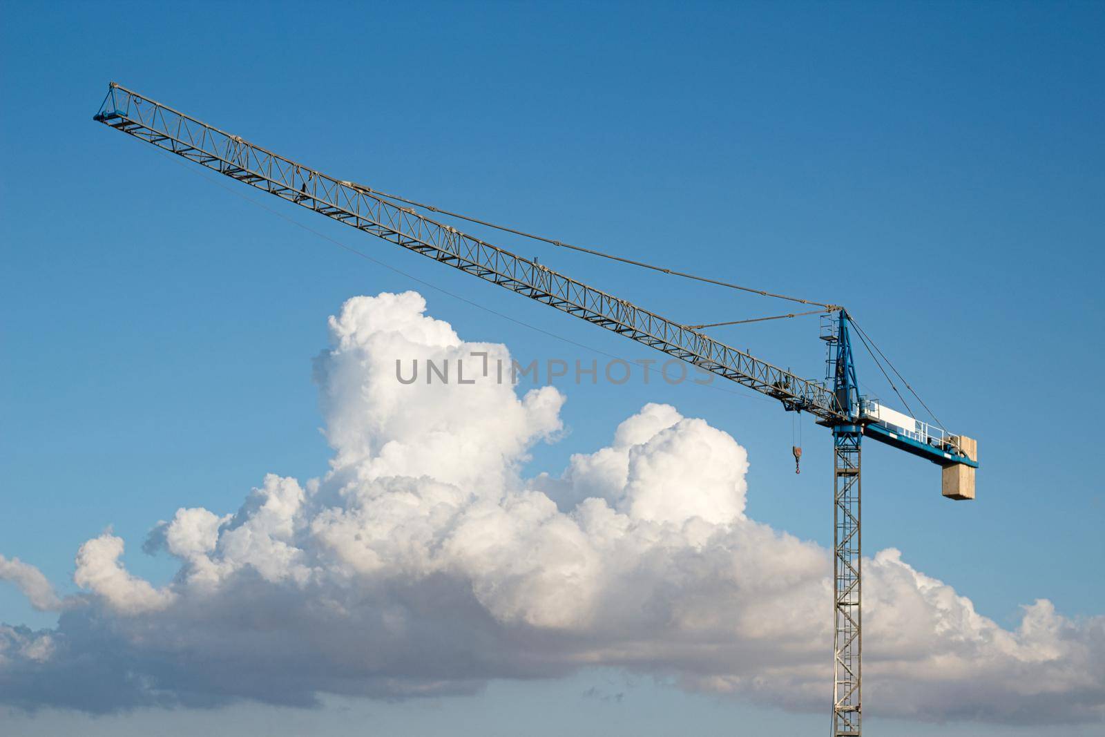 Industrial construction tower crane against a blue sky background with dramatic clouds