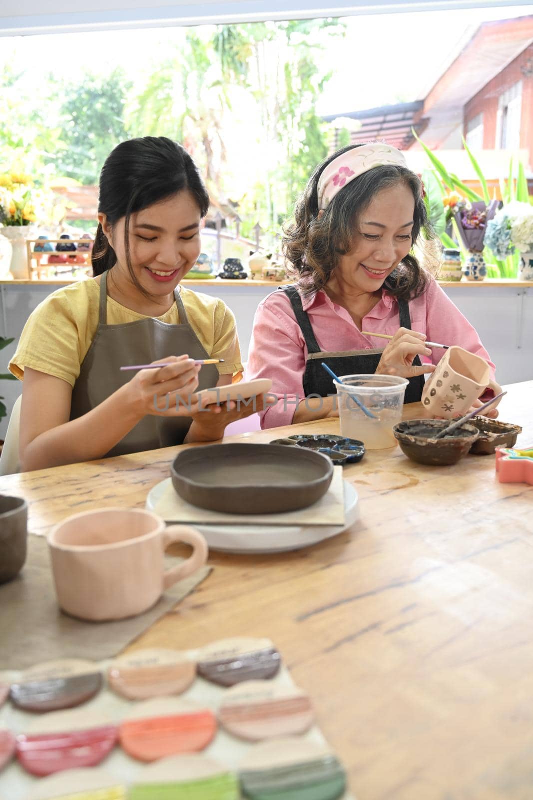Middle aged woman and young woman making ceramics in craft studio workshop. Activity, handicraft, hobbies concept by prathanchorruangsak