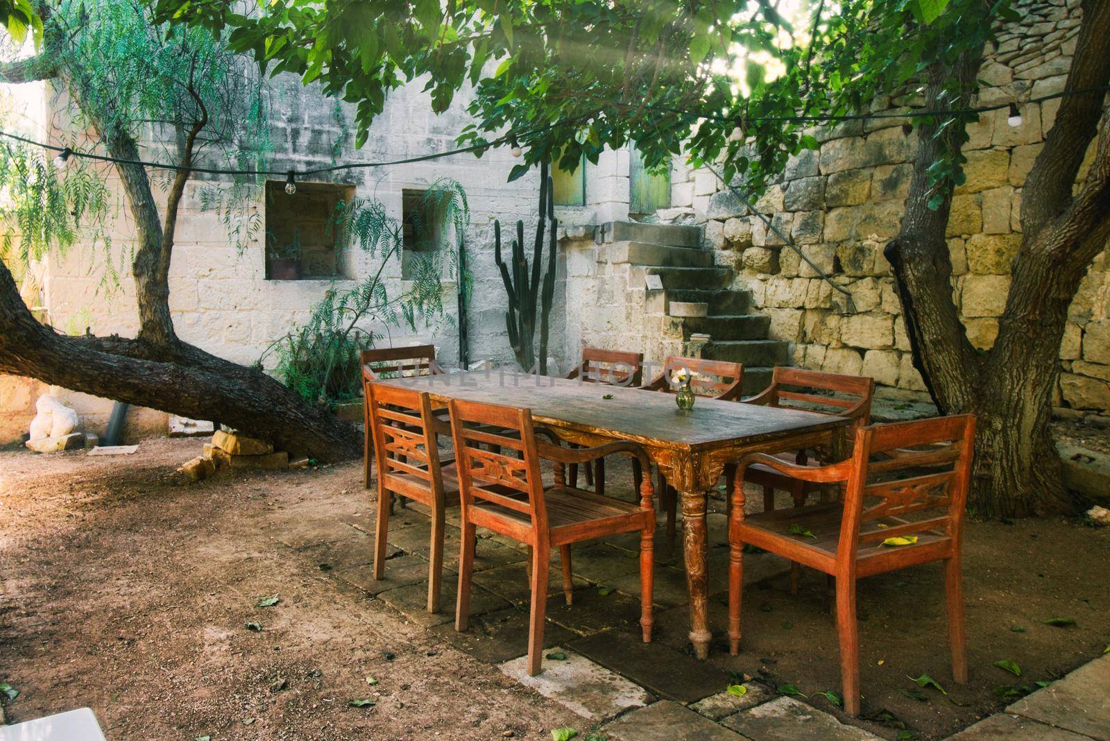 Old-fashioned wooden dining table and chairs outdoors in a Mediterranean garden by tennesseewitney