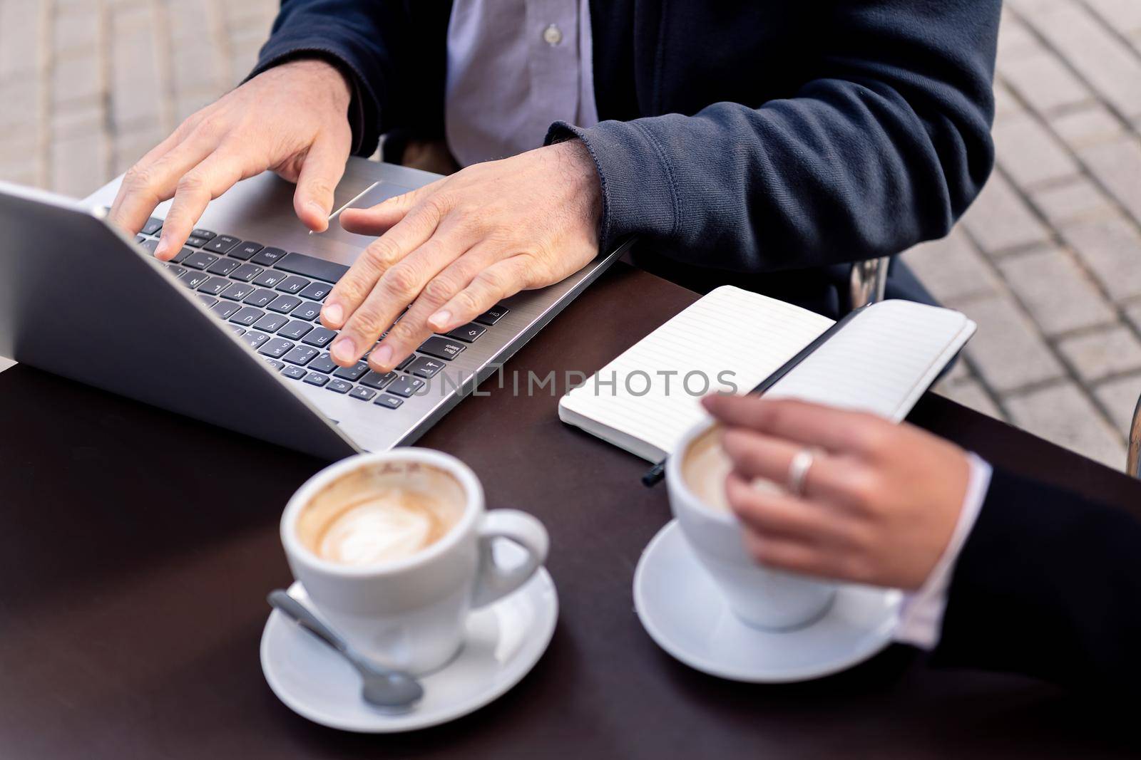 detail of a man's hands working with his laptop computer on a terrace of a coffee shop in the financial district, concept of entrepreneurship and business