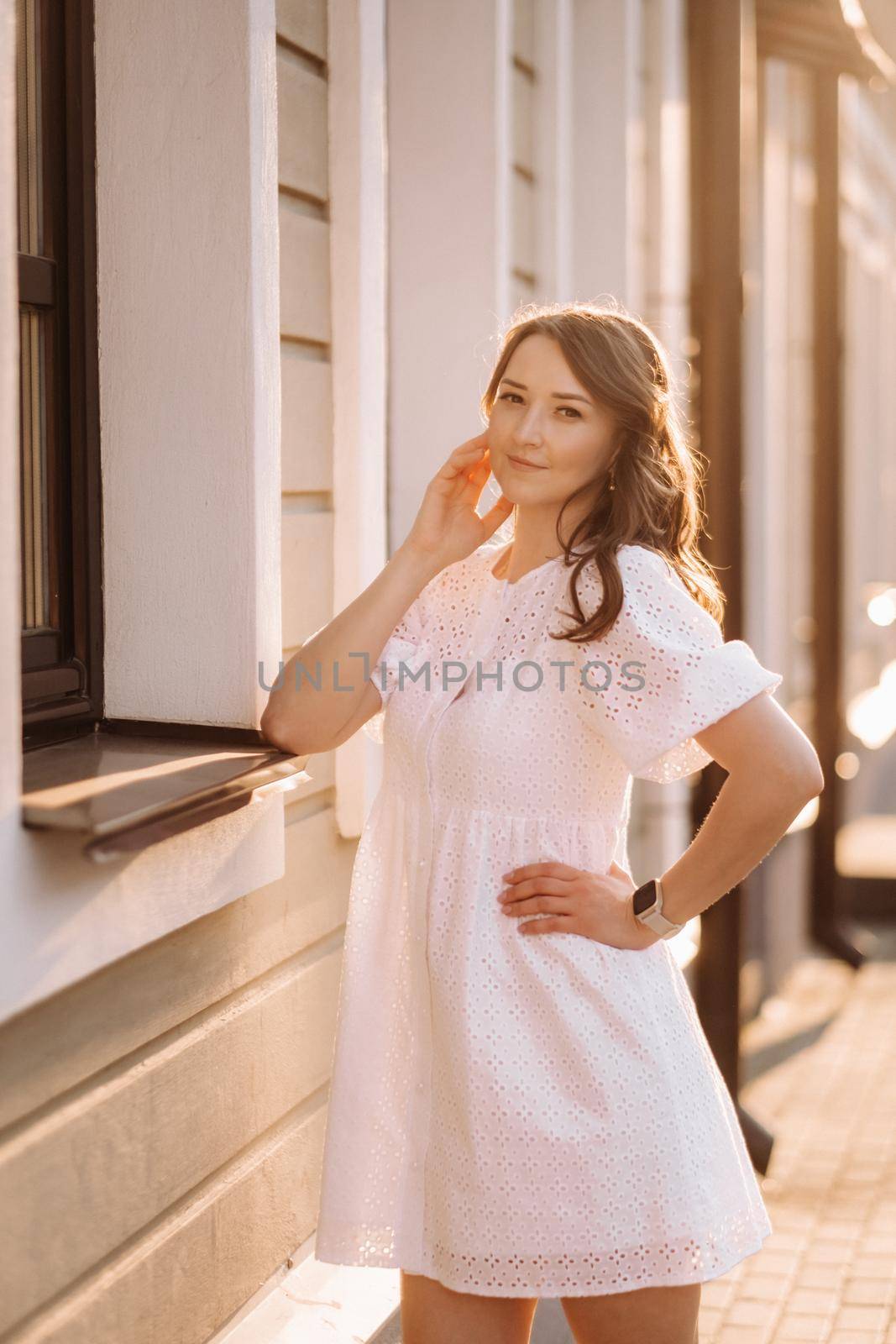 A beautiful woman in a white dress at sunset in the city. Evening street photography by Lobachad