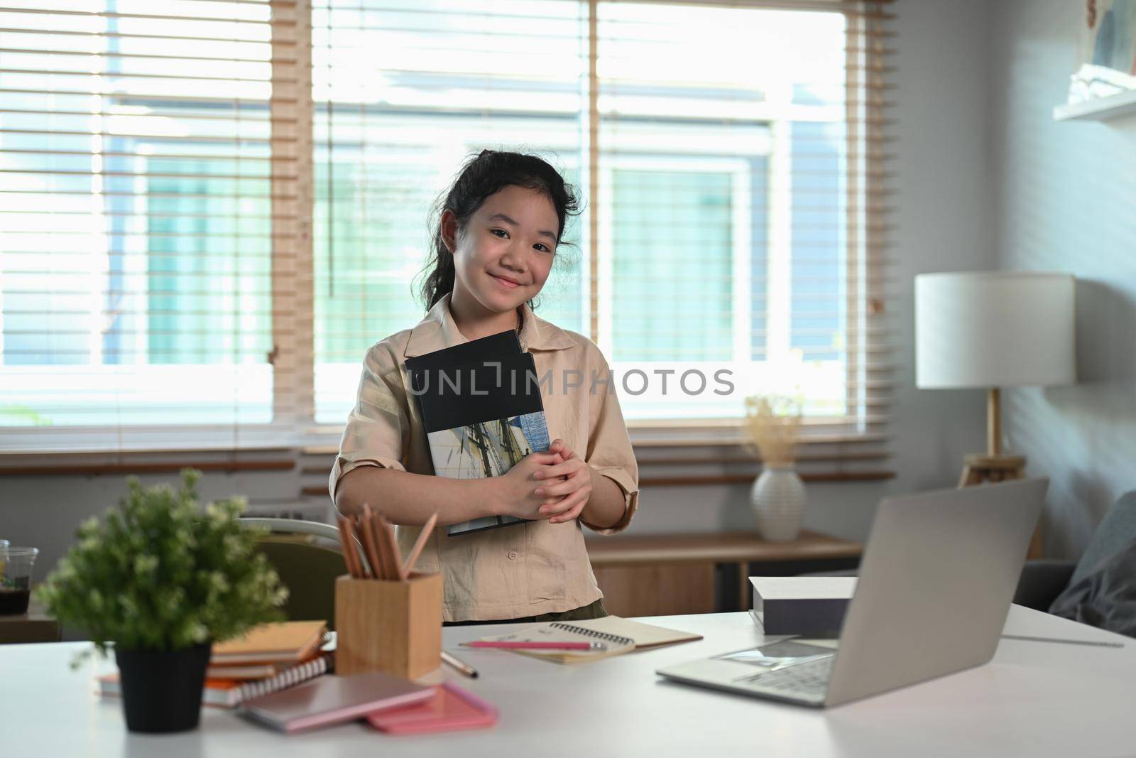 Cheerful asian girl holding book and smiling at camera.