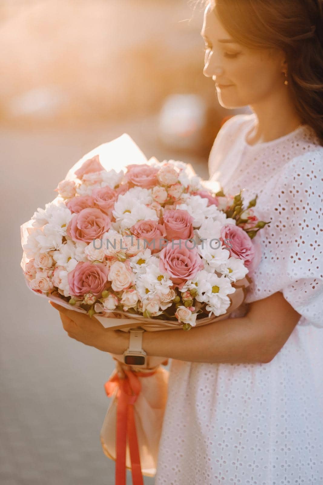 A happy woman in a white dress at sunset with a bouquet of flowers in the city by Lobachad