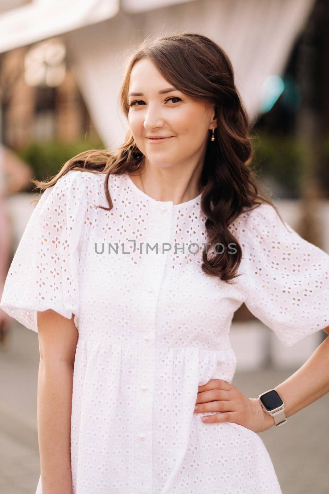 A beautiful woman in a white dress at sunset in the city. Evening street photography by Lobachad