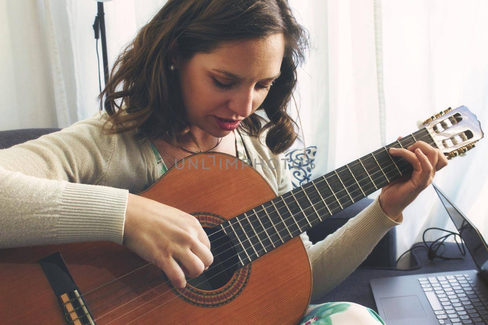 Attractive young lady playing and recording music using a Spanish classical guitar and a laptop