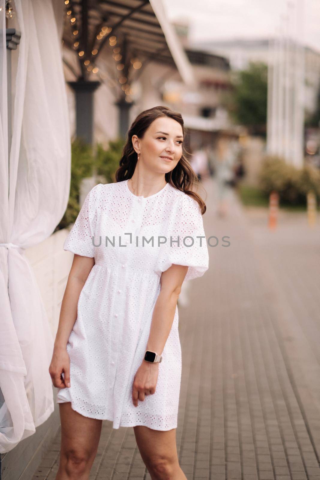 A beautiful woman in a white dress at sunset in the city. Evening street photography.