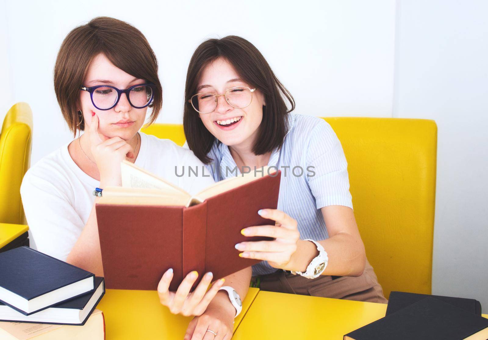 Two female students having fun reading text books in class by tennesseewitney